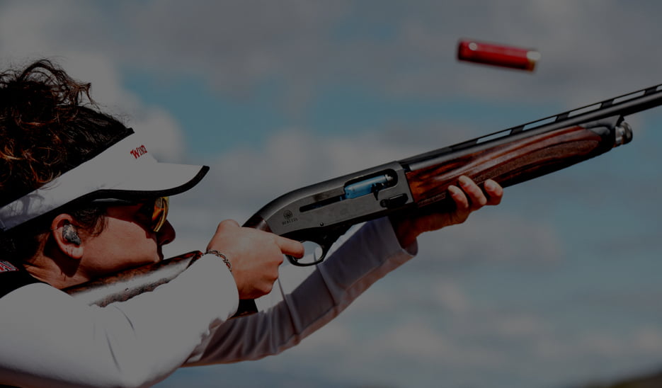 Side view of a competitive female shooter in the act of shooting as a shotshell cartridge is expelled