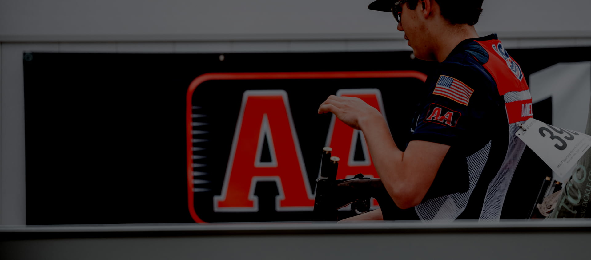 Competitive shooter loading shotgun rounds into a gun in front of a large Winchester AA ammo banner.